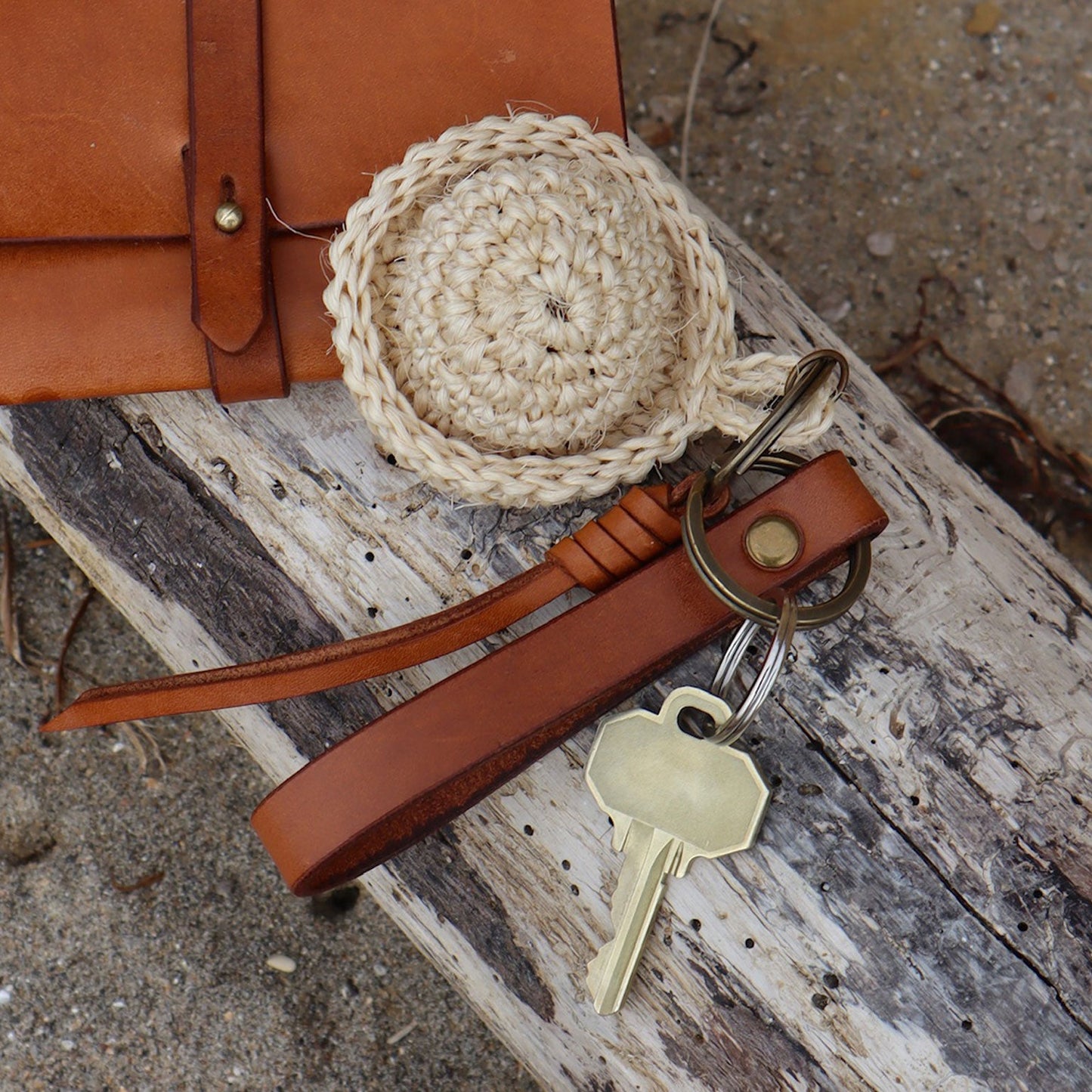 Brown leather belt with a woven belt buckle and keychain on a textured surface