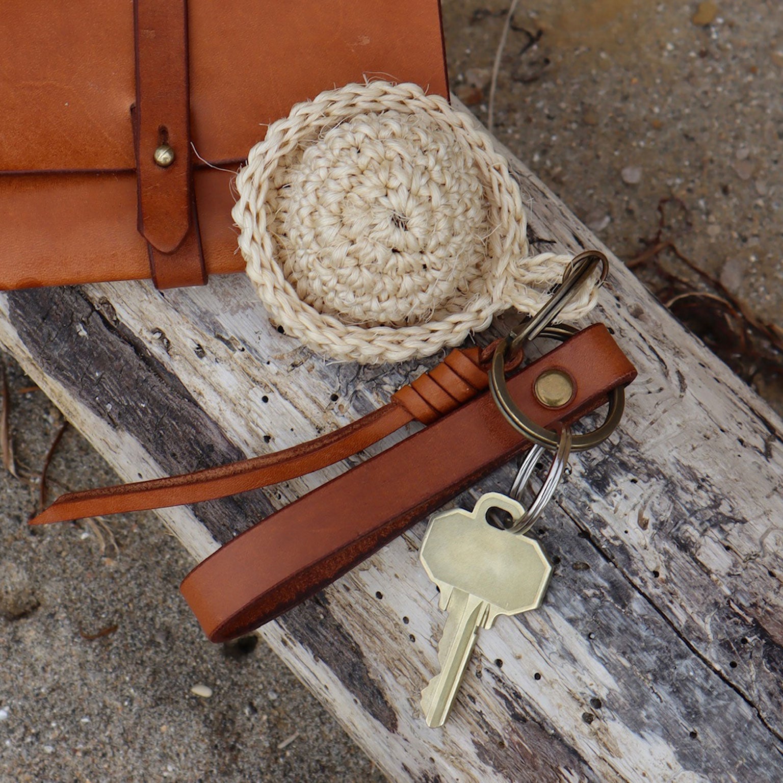 Brown leather belt with a woven belt buckle and keychain on a textured surface