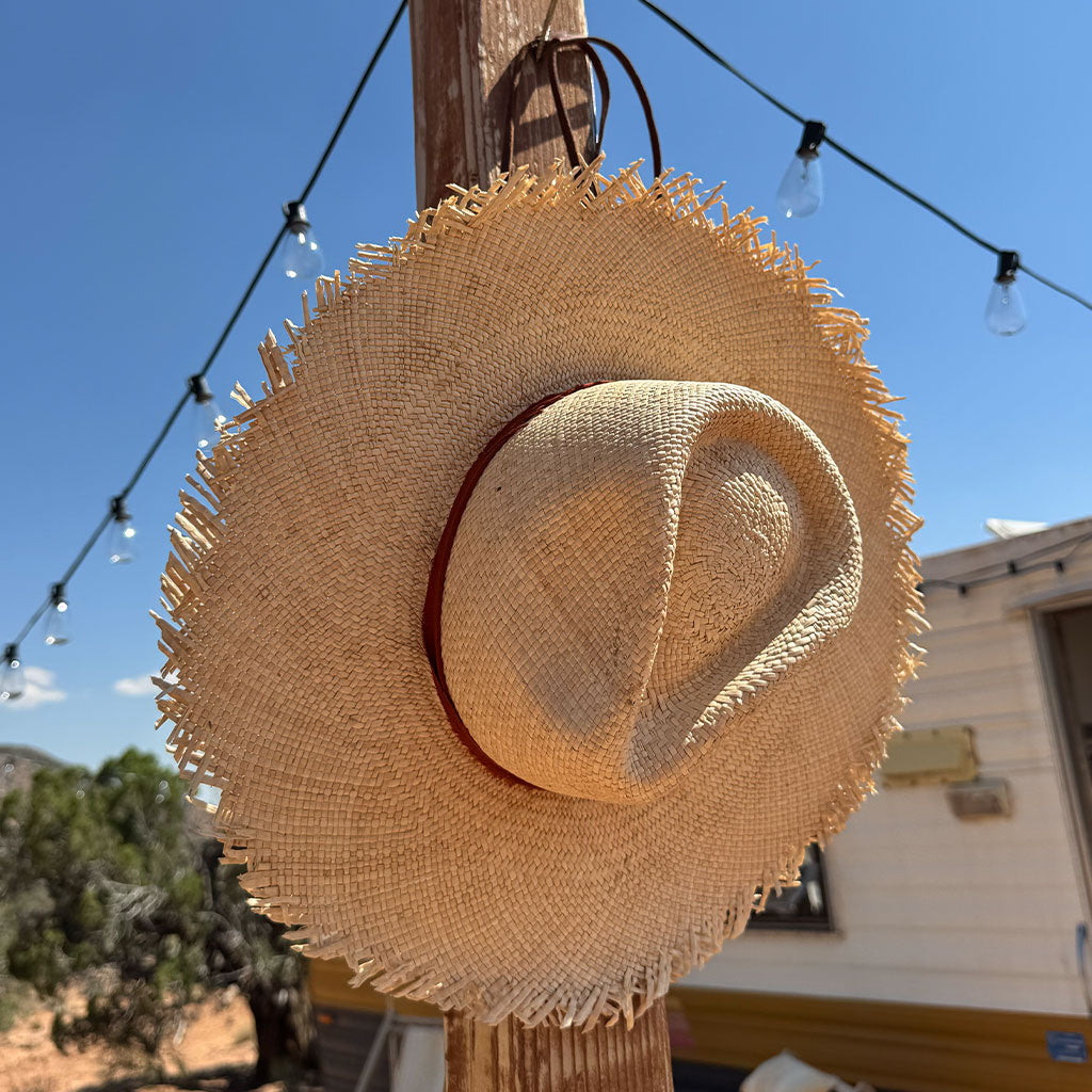 Woven straw hat hanging on a wooden post against a blue sky.