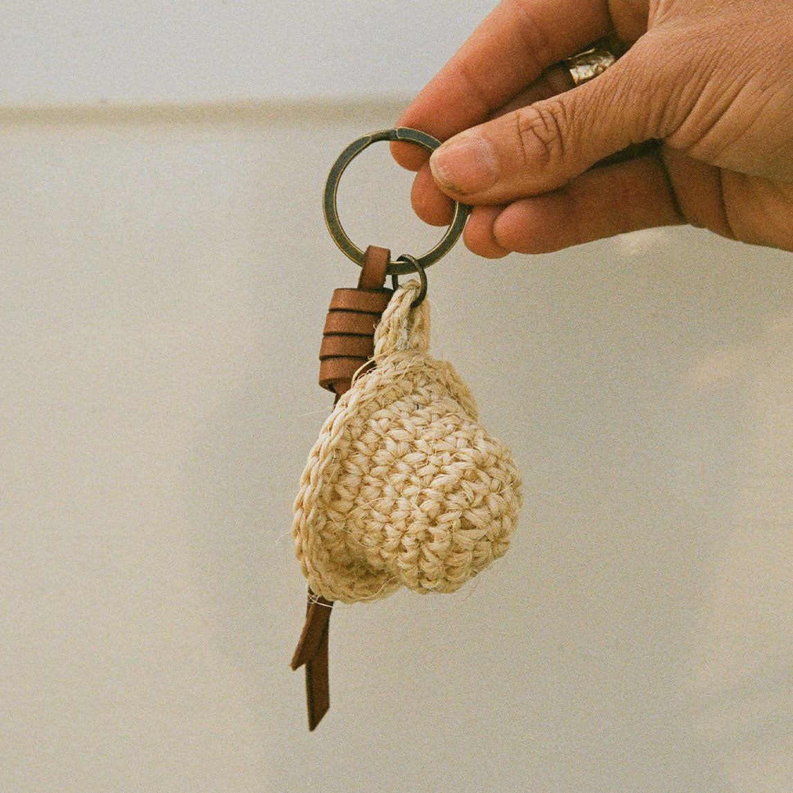 Hand holding a keychain with a crocheted pear-shaped charm against a neutral background